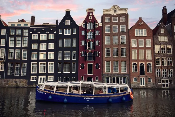 Blaues Grachtenboot auf dem Wasser mit traditionellen Häusern im Hintergrund