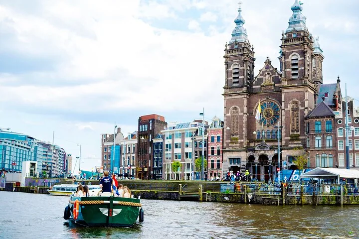 Grünes Grachtenboot fährt vor einer Amsterdamer Kirche vorbei