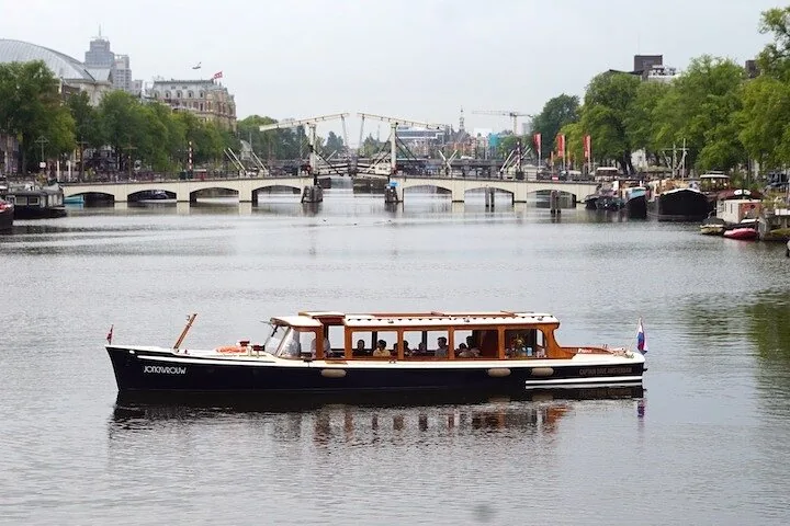 Klassisches Grachtenboot auf dem Wasser mit der Magere Brug im Hintergrund